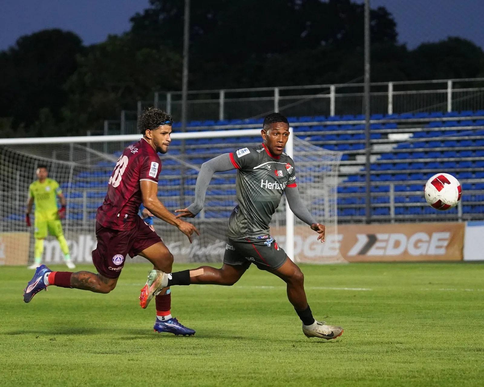 Jugadores corriendo tras el balón al atardecer