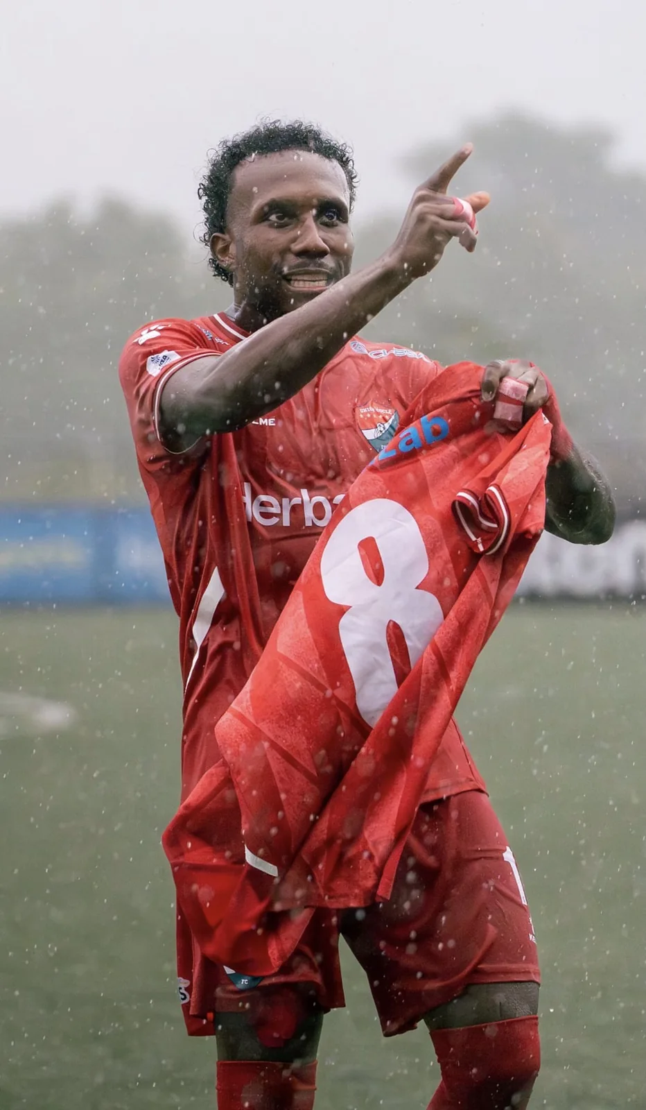 Jugador de rojo con el número 8 bajo la lluvia, señalando con su camiseta en la mano