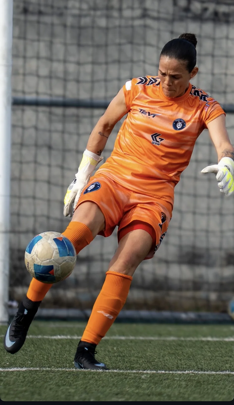Portera de naranja despejando el balón con el pie