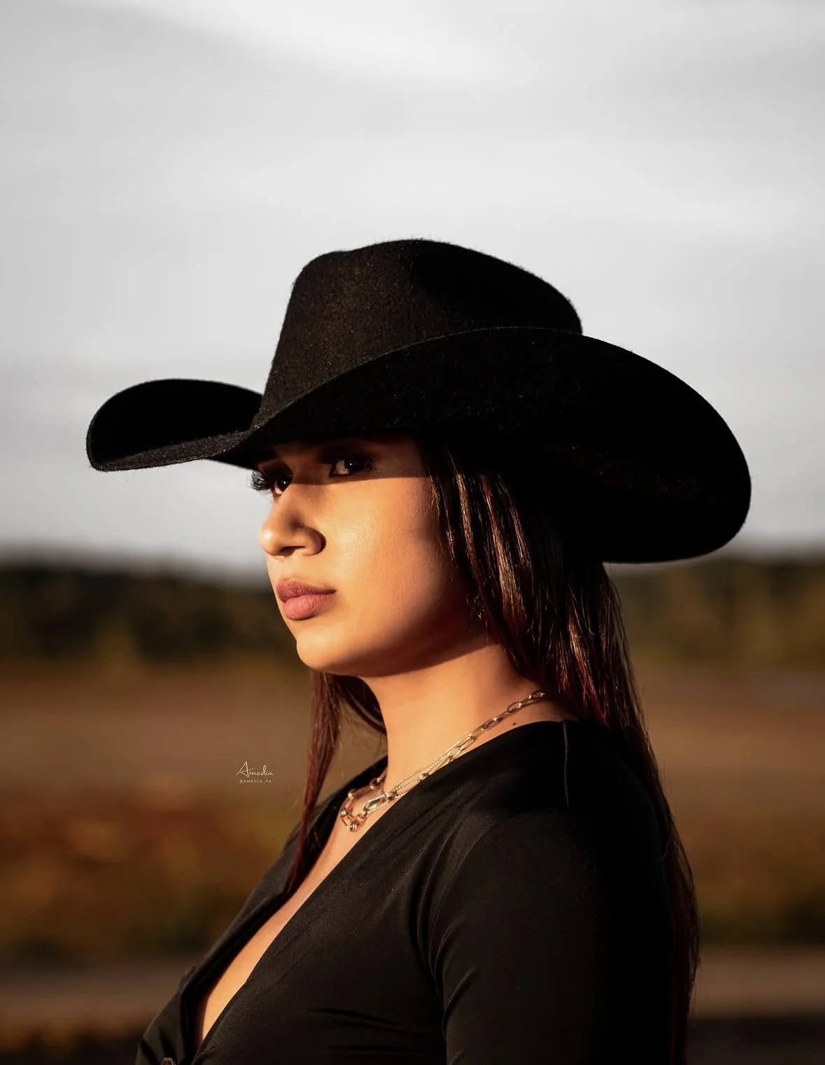 Joven de perfil con sombrero vaquero negro y collar de cadena, luz del atardecer