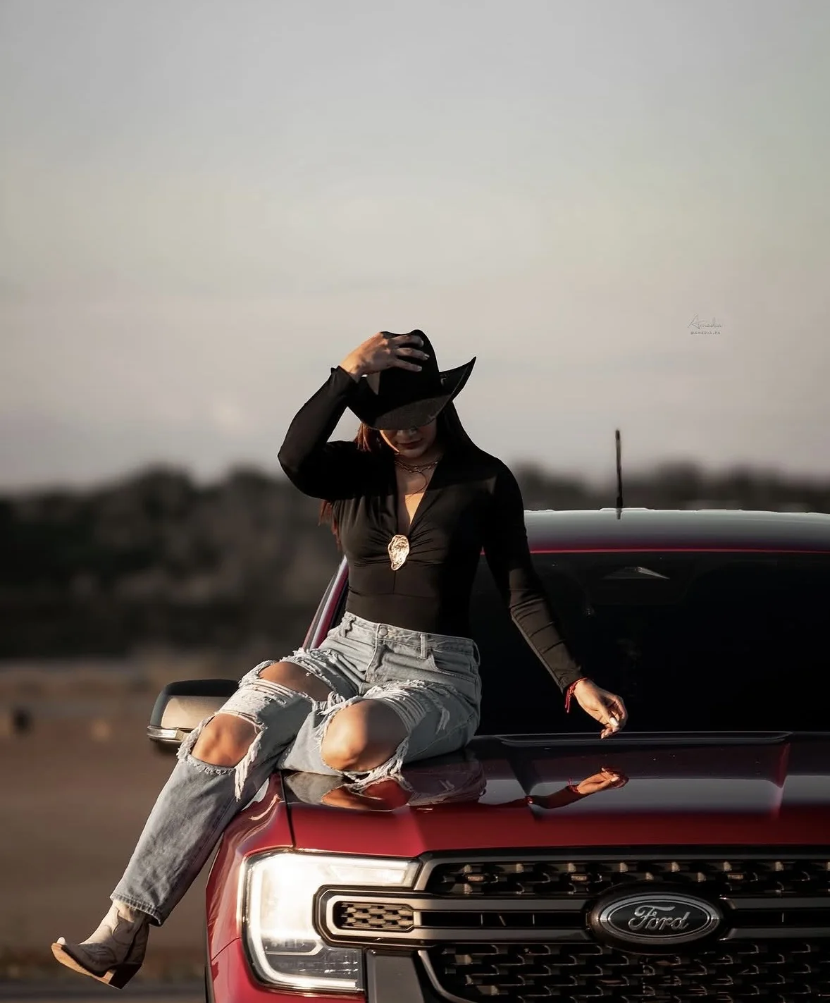 Joven con sombrero vaquero sentada sobre el capó de una camioneta roja