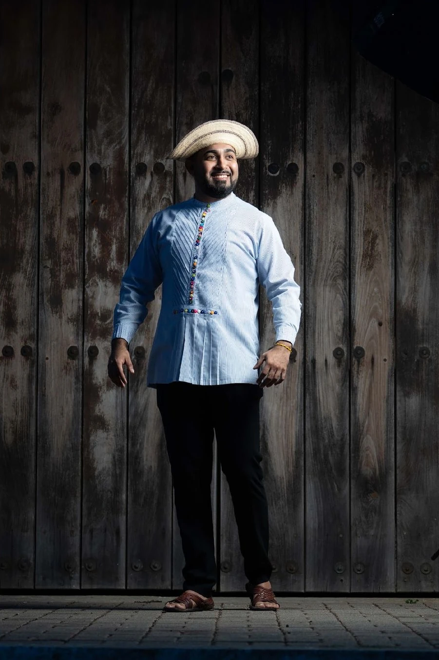 Mario con camisa montuna celeste y sombrero típico, frente a un portón de madera