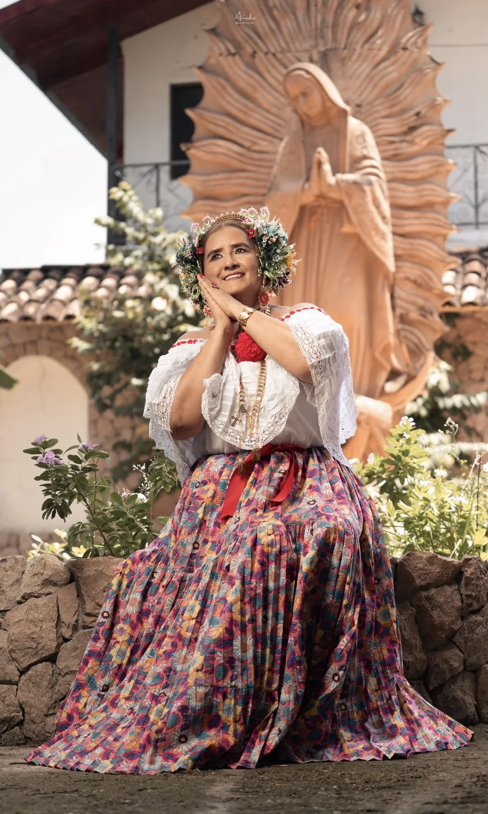 Señora con pollera floreada y flores en el cabello, frente a una imagen de la Virgen